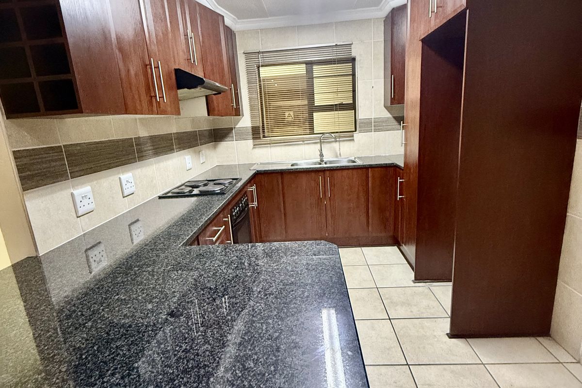 A functional kitchen featuring dark wood cabinetry, granite countertops, a built-in hob with extractor, and tiled flooring throughout.
