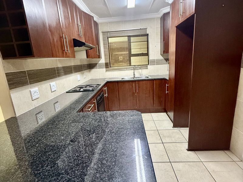 A functional kitchen featuring dark wood cabinetry, granite countertops, a built-in hob with extractor, and tiled flooring throughout.