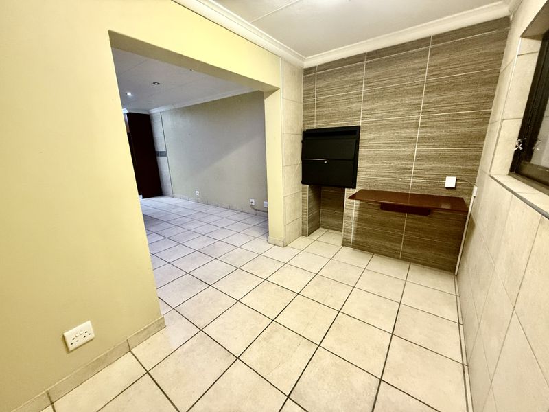 An empty covered patio area featuring tiled flooring, wall cladding, and a built-in braai, providing a functional space for outdoor entertaining.