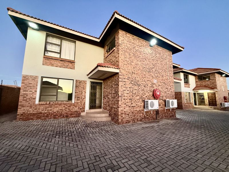 Exterior view of a face brick apartment complex featuring a paved driveway, security gates, and mounted air conditioning units.