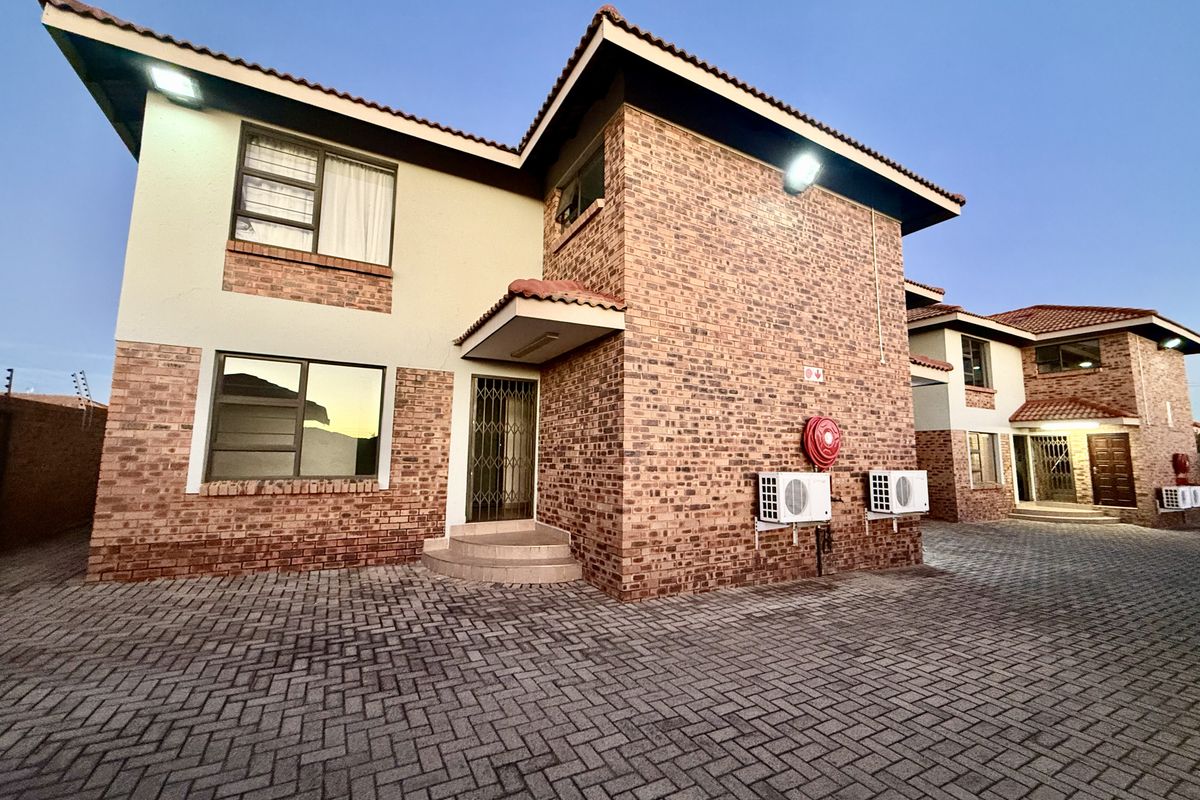 Exterior view of a face brick apartment complex featuring a paved driveway, security gates, and mounted air conditioning units.