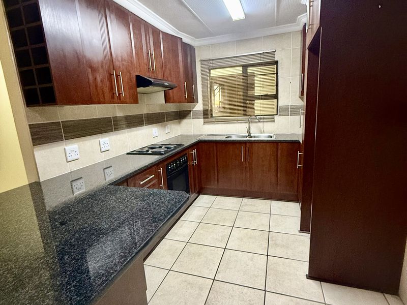 A functional kitchen featuring dark wood cabinetry, granite countertops, built-in oven, electric hob, and tiled flooring with a neutral backsplash.