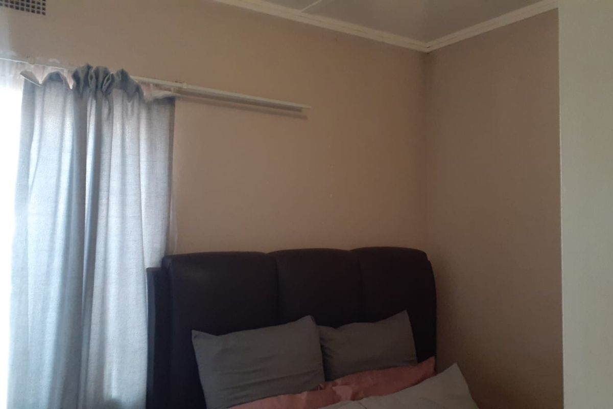 A bedroom interior featuring neutral wall paint, a cornice detail, and a curtain rail.