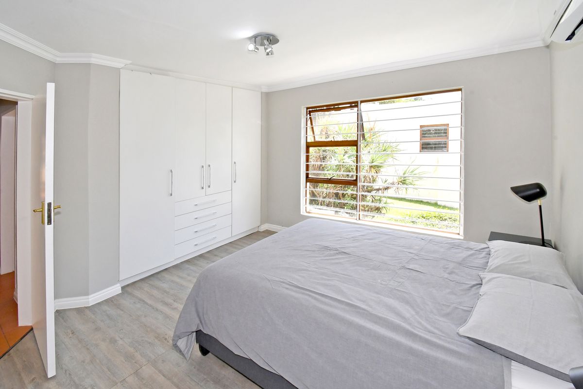 A well-maintained bedroom featuring built-in cupboards, light laminate flooring, and an air conditioning unit, offering a clean and functional living space.