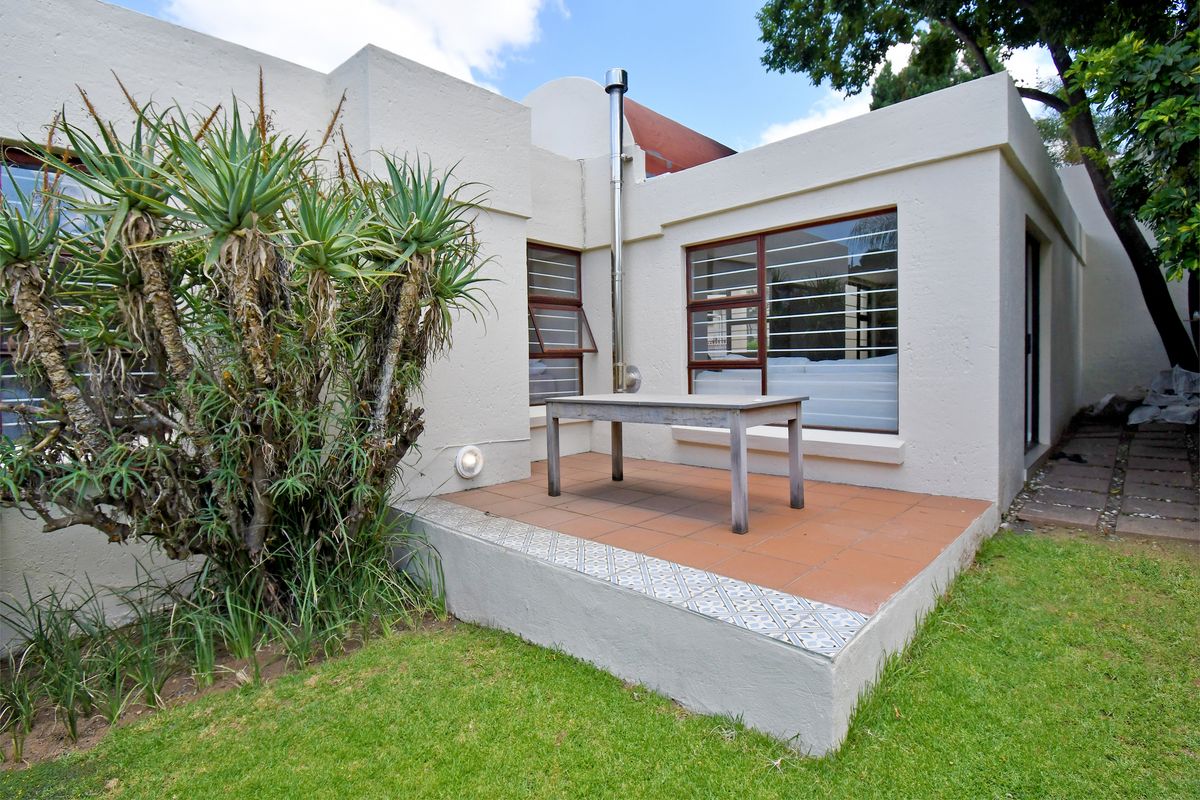 Rear exterior view of the townhouse featuring a tiled patio area, external fireplace flue, and security-fitted windows overlooking a small garden.