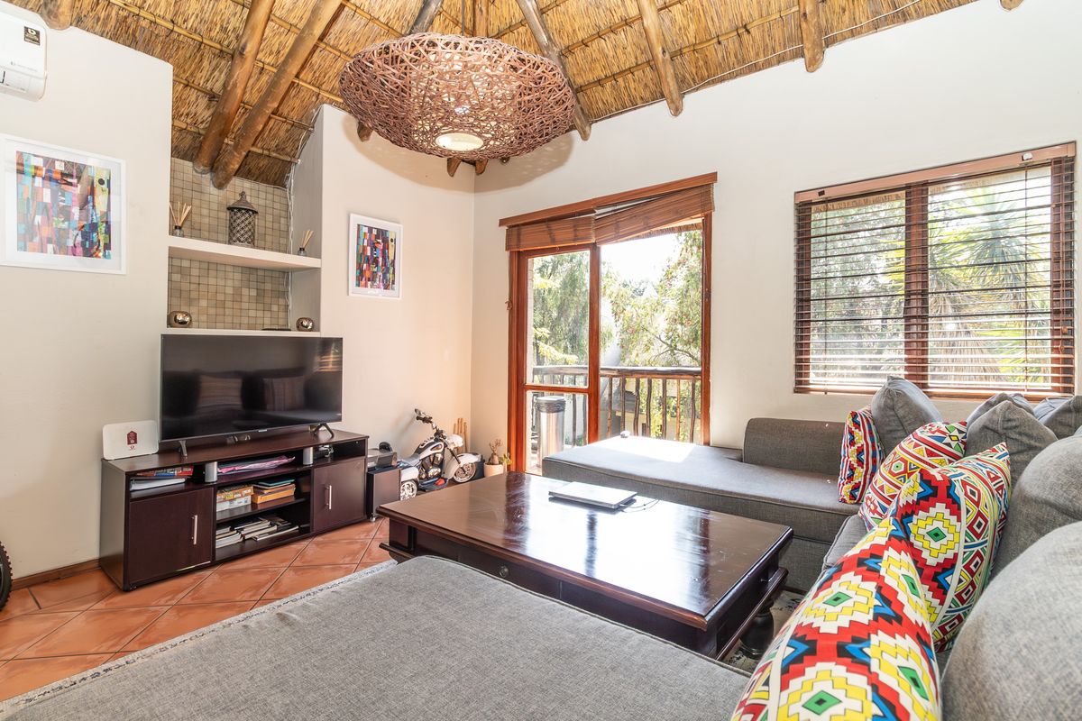 Cozy living room featuring a high thatched ceiling with exposed timber rafters, terracotta flooring, and direct access to a balcony through sliding glass doors.