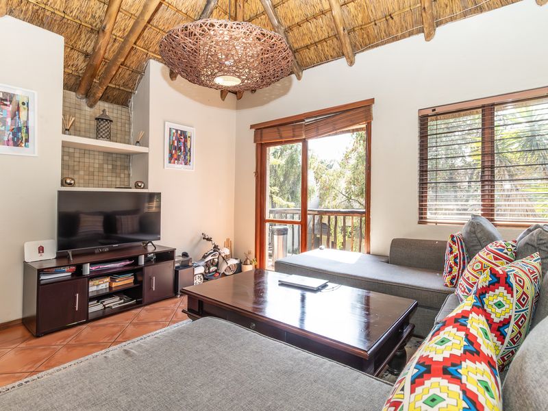Cozy living room featuring a high thatched ceiling with exposed timber rafters, terracotta flooring, and direct access to a balcony through sliding glass doors.
