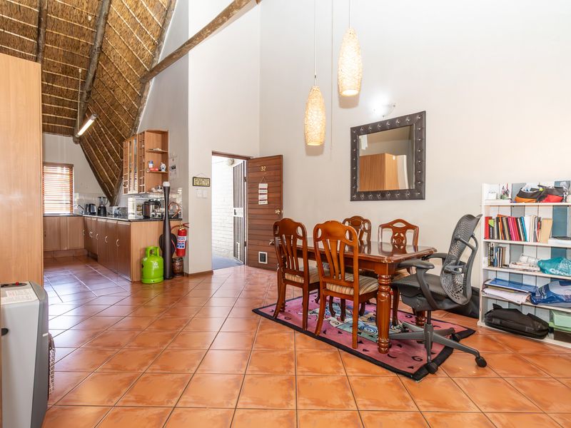 Open-plan living and kitchen area featuring high vaulted thatched ceilings, exposed timber beams, and ceramic tiled flooring with direct access to the entrance.