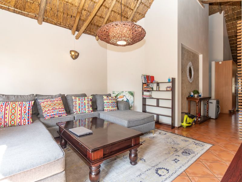 A living room featuring a high vaulted thatched ceiling with exposed timber rafters and terracotta floor tiles, creating a rustic and spacious atmosphere.