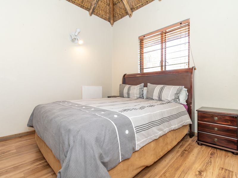 A cozy bedroom featuring a unique thatched ceiling, laminate flooring, and a window with fitted venetian blinds.
