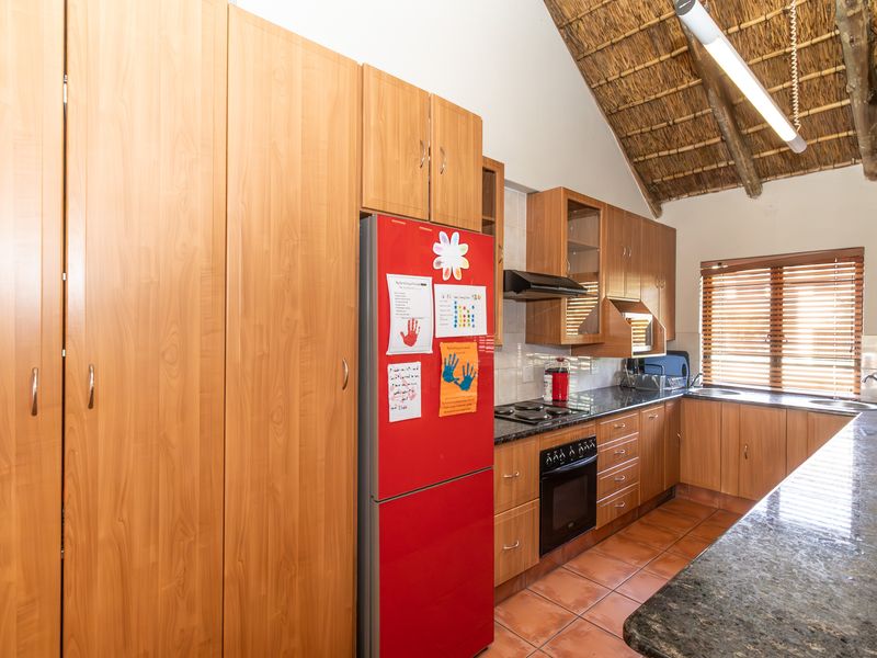 A kitchen featuring wooden cabinetry, granite countertops, built-in appliances, and a distinctive vaulted thatched roof ceiling with exposed timber beams.