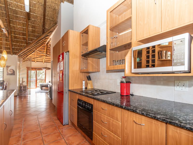 Open-plan kitchen featuring wooden cabinetry, granite countertops, and built-in appliances, set under a high vaulted thatched ceiling.
