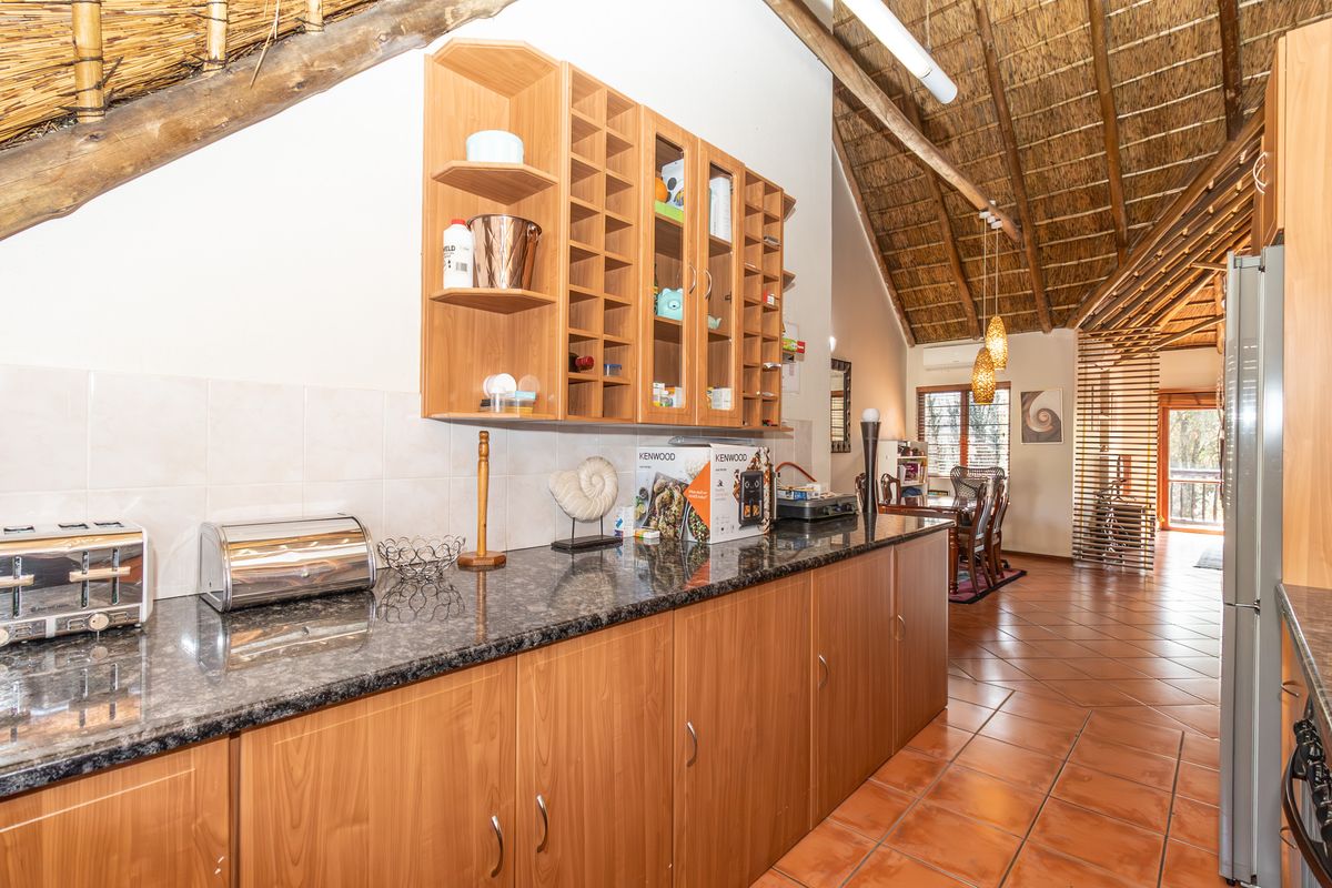 A kitchen area featuring granite countertops, laminate cabinetry, and a distinctive thatched roof with exposed timber beams, flowing into an open-plan living space.