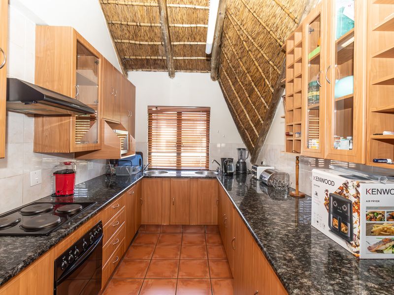 A functional kitchen featuring granite countertops, built-in wooden cabinetry, an electric hob, and a unique vaulted thatched roof ceiling.