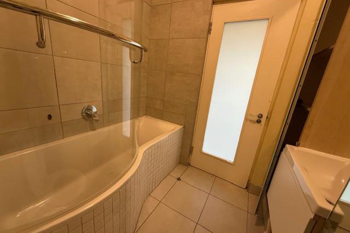 A functional bathroom featuring a curved bathtub with a glass shower screen, tiled walls, and a frosted glass door.