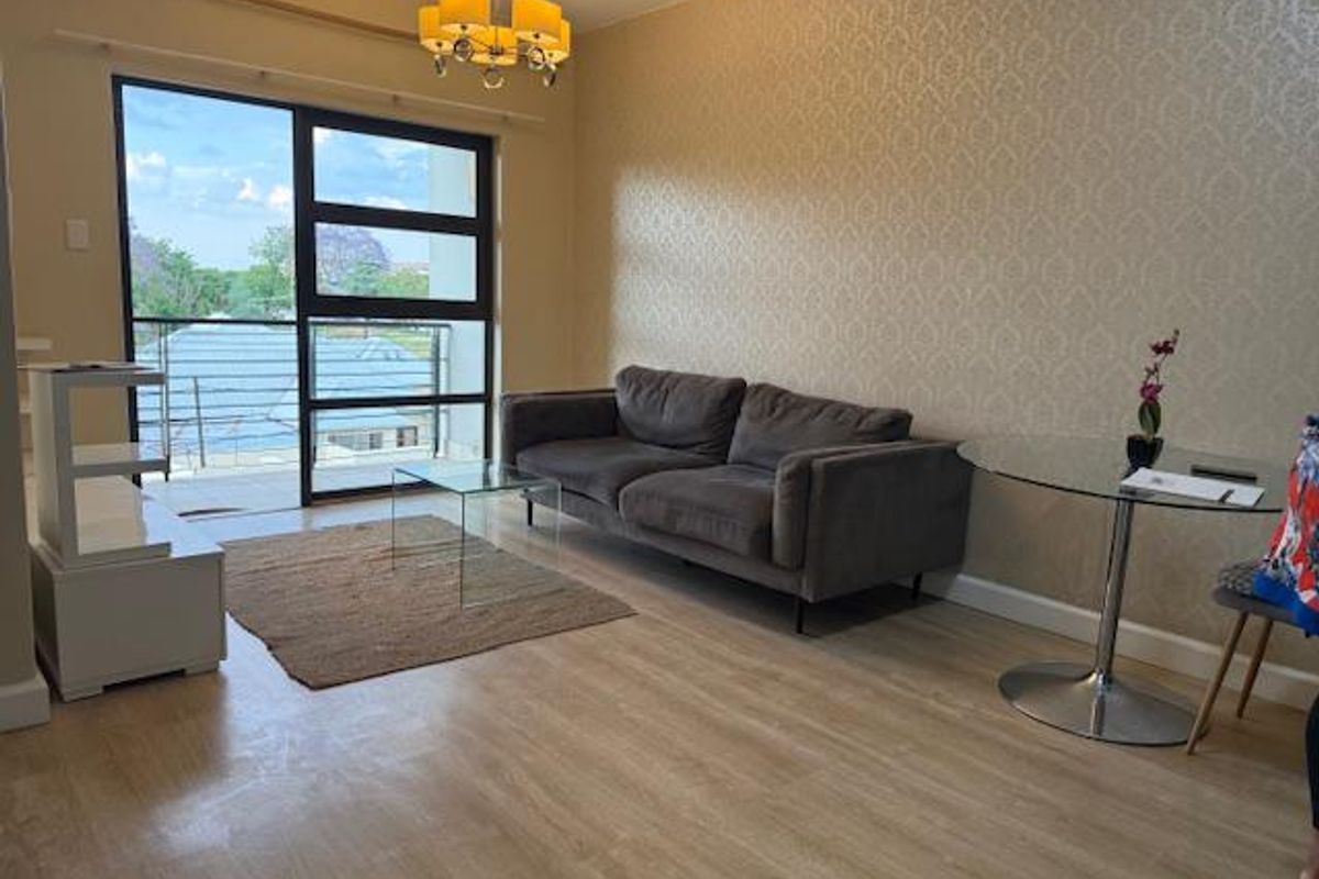 A bright living room featuring light wood-look flooring, textured wallpaper, and large sliding glass doors opening onto a balcony.