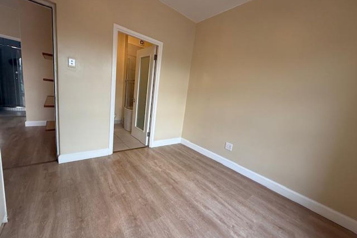 A bright, empty bedroom featuring light wood-look laminate flooring, neutral wall tones, and direct access to an adjoining bathroom.