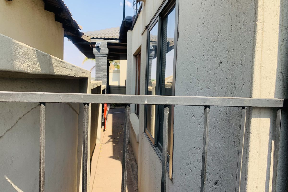 A narrow side passage or rear exterior walkway featuring paved flooring, metal balustrades, and aluminium window frames along the townhouse exterior.