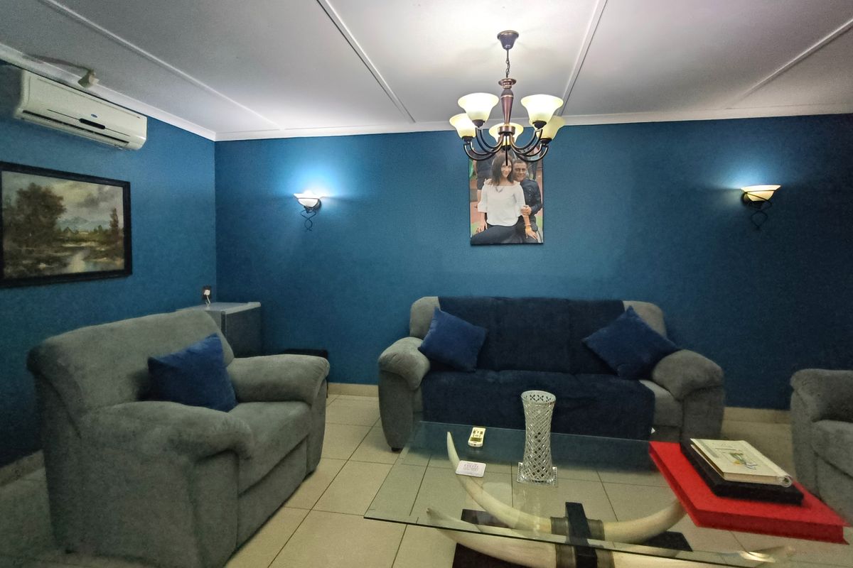 A living room featuring blue accent walls, tiled flooring, wall sconces, a central chandelier, and a wall-mounted air conditioning unit.