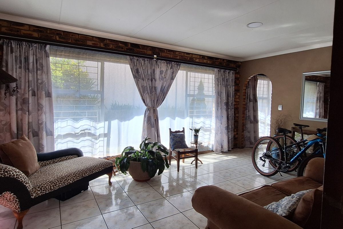 A spacious living room featuring exposed brick walls, large windows with security bars, and tiled flooring, offering a rustic and well-lit living space.