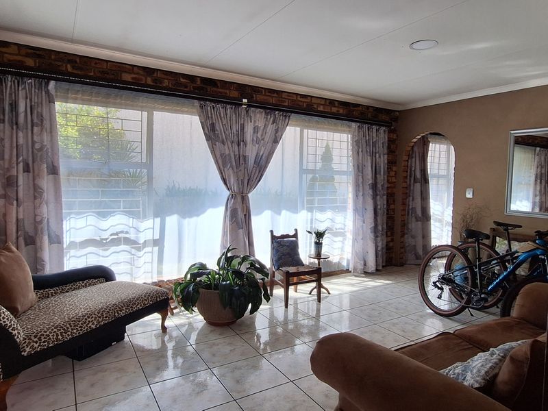 A spacious living room featuring exposed brick walls, large windows with security bars, and tiled flooring, offering a rustic and well-lit living space.
