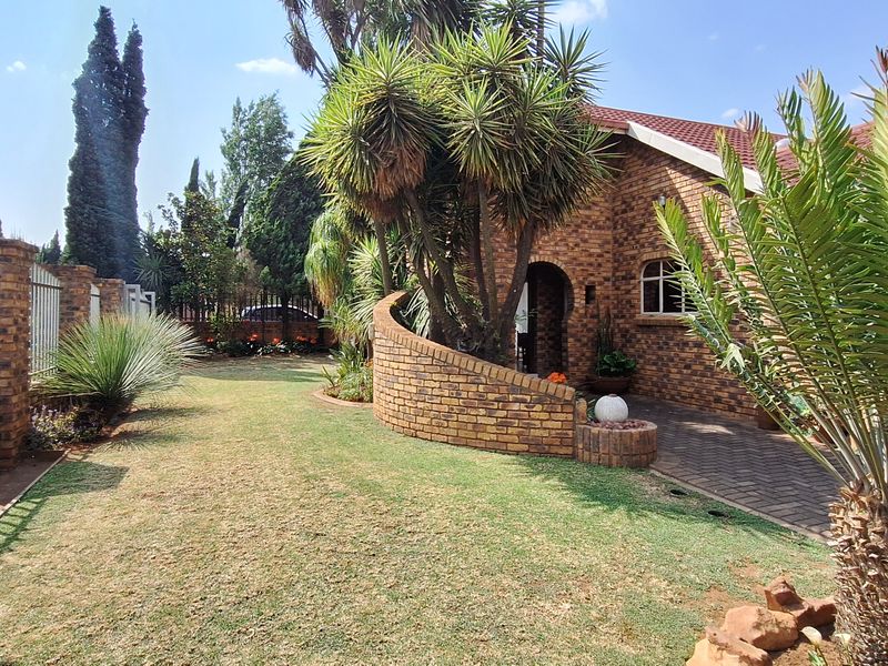 Front exterior view of a face brick house featuring a paved driveway, arched entrance, and established garden with brick boundary walls and metal fencing.