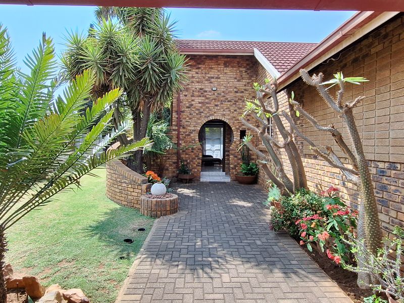A well-maintained front entrance featuring a brick facade, a paved walkway leading to an arched doorway, and established garden landscaping.