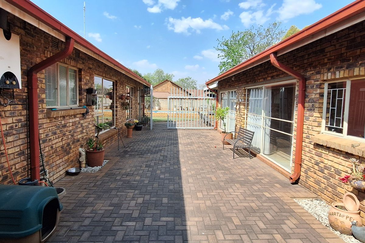A paved rear courtyard area between two brick building wings, featuring a wall-mounted gas geyser and sliding door access.