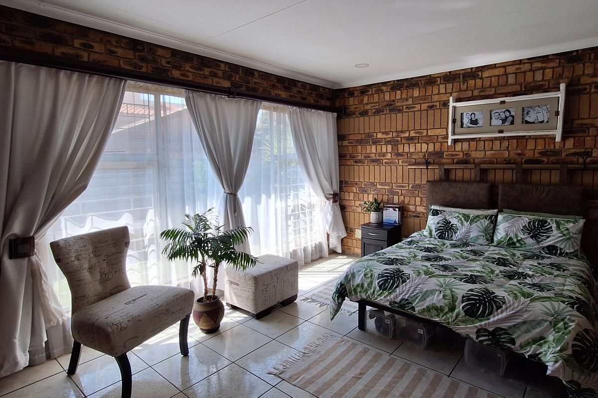 Spacious bedroom featuring exposed brick walls, tiled flooring, and a large sliding glass door providing ample natural light.