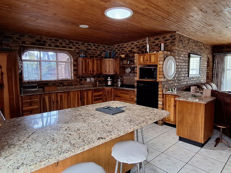 Spacious open-plan kitchen and living area featuring exposed brick walls, timber ceilings, granite countertops, and ample wooden cabinetry.