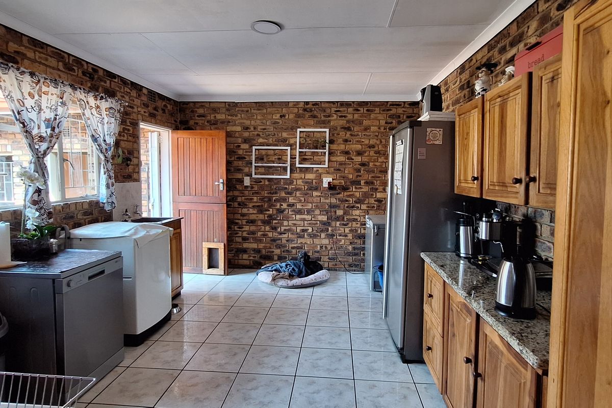 A functional kitchen featuring exposed brick walls, wooden cabinetry, granite countertops, and tiled flooring with direct access to the exterior.