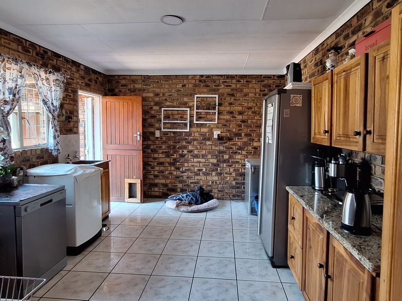 A functional kitchen featuring exposed brick walls, wooden cabinetry, granite countertops, and tiled flooring with direct access to the exterior.