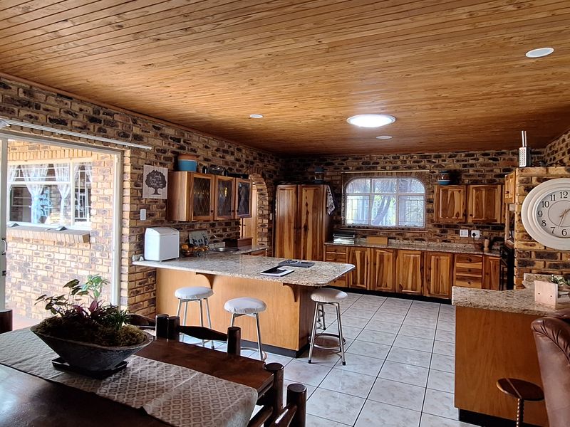 Spacious open-plan kitchen and living area featuring exposed brick walls, warm timber ceilings, granite countertops, and a functional kitchen island with breakfast bar seating.