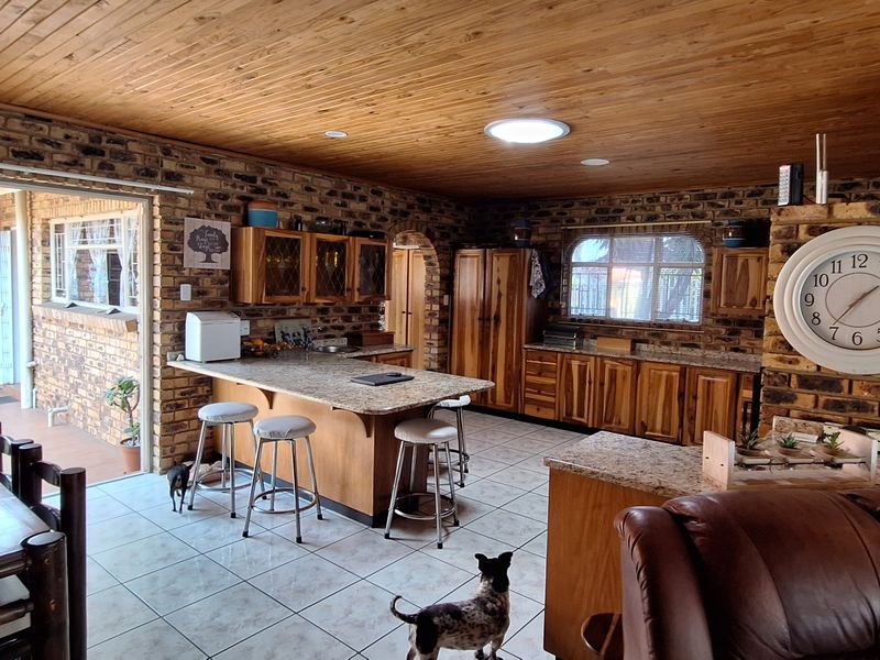 Spacious open-plan kitchen and living area featuring exposed brick walls, timber ceiling, granite countertops, and direct access to an outdoor patio.