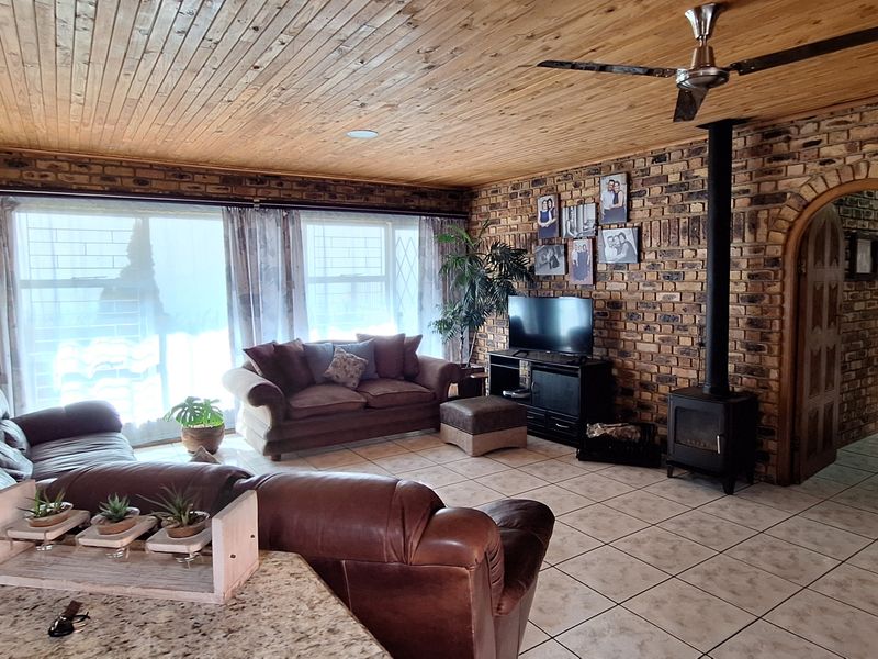 Spacious living room featuring exposed brick walls, a timber ceiling, ceramic floor tiles, and a cozy freestanding wood-burning fireplace.