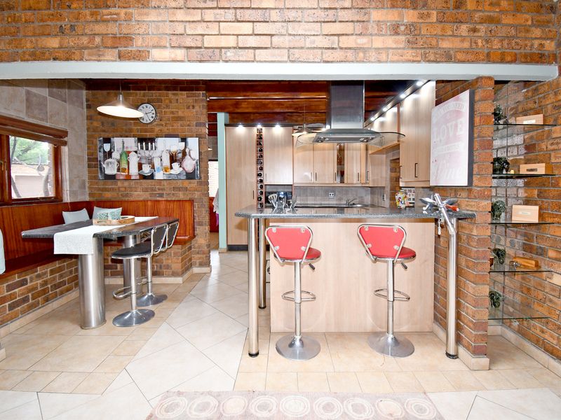 A rustic kitchen featuring exposed brick walls, built-in cabinetry with granite countertops, a stainless steel extractor fan, and a cozy built-in breakfast nook.