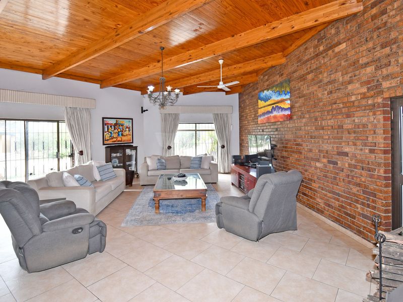 Spacious living room featuring an exposed timber beam ceiling, a prominent brick feature wall, tiled flooring, and large sliding glass doors providing natural light.