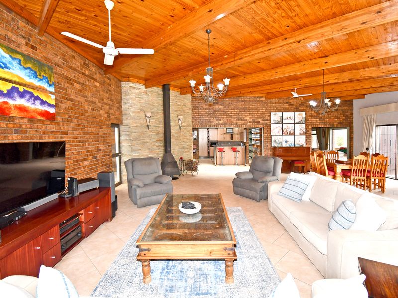 Spacious open-plan living and dining area featuring exposed timber beam ceilings, brick feature walls, and a stone fireplace, creating a warm, rustic atmosphere.