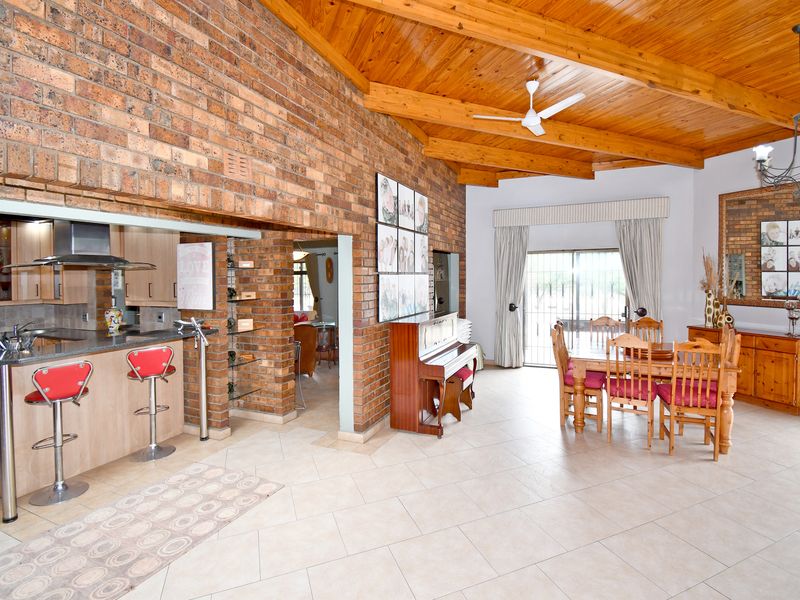 Spacious open-plan living and dining area featuring a timber raked ceiling, exposed brick feature wall, and an integrated kitchen with granite countertops.