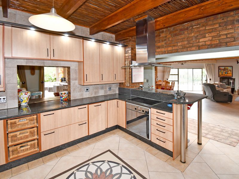 A well-appointed kitchen featuring light wood cabinetry, granite countertops, built-in appliances, and a rustic aesthetic with exposed brick walls and timber ceiling beams.