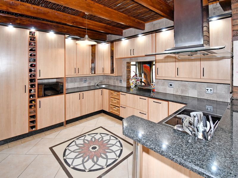 A well-appointed kitchen featuring light wood cabinetry, granite countertops, a built-in wine rack, and a distinctive exposed timber beam ceiling.