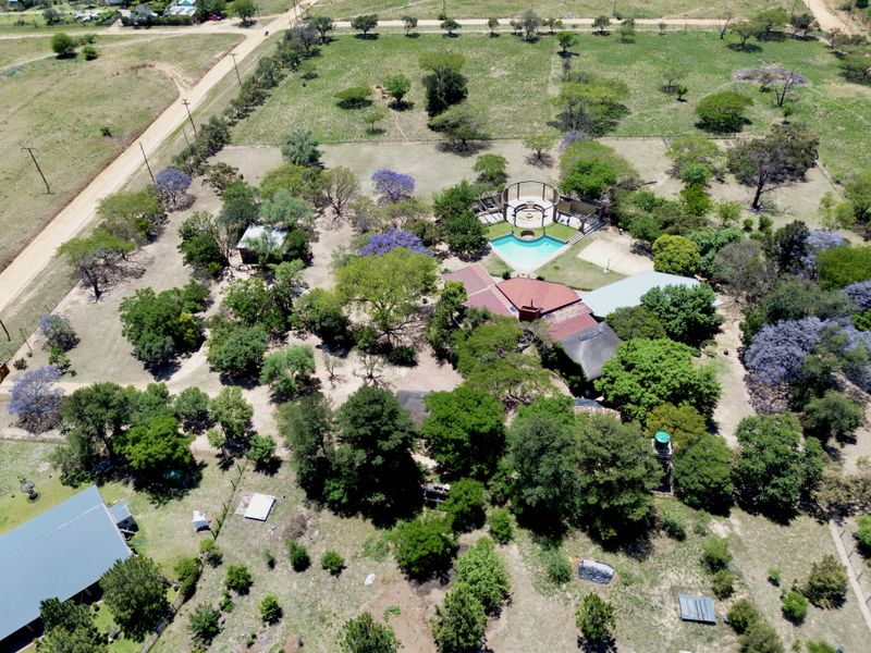 Aerial view of a large property featuring a swimming pool, outdoor entertainment area, mature trees, and expansive grounds.