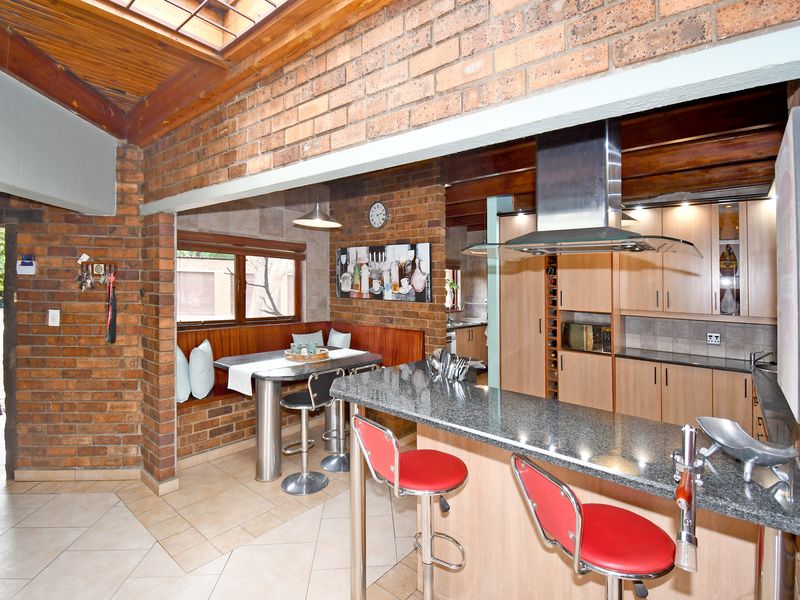 Open plan kitchen and dining area featuring exposed brick walls, timber beam ceilings, a skylight, and a granite breakfast bar.