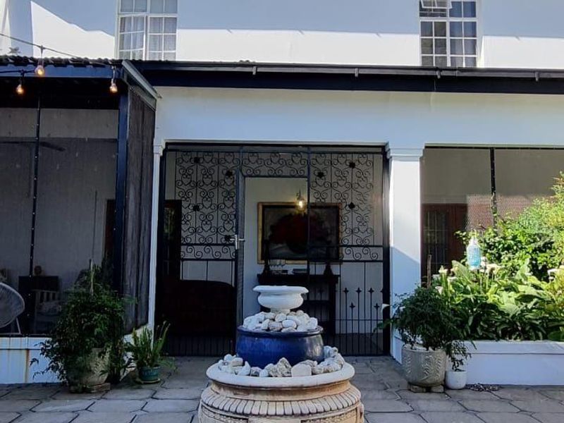A well-maintained rear patio featuring stone paving, a decorative fountain, and a covered entertainment area with wrought iron security gates.