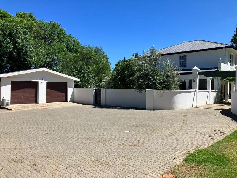 Front view of the property featuring a paved driveway, a double garage, and a well-maintained boundary wall leading to the main residence.