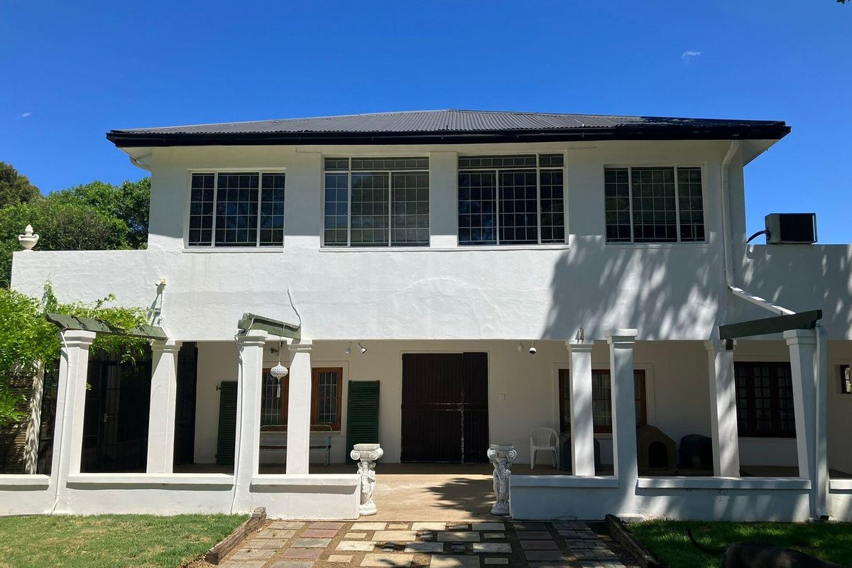Rear elevation of a two-story farmhouse featuring a covered patio, grid-pattern windows, and a stone-paved walkway leading to the entrance.