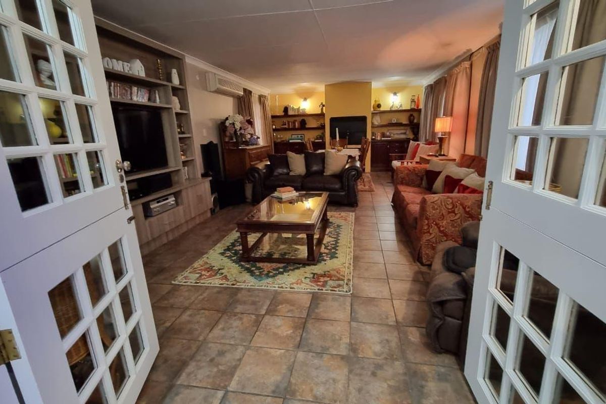 Spacious living room featuring tiled flooring, built-in cabinetry, a fireplace, and split-system air conditioning, accessed through classic French doors.
