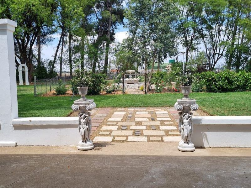 A covered patio area overlooking a landscaped garden with a stone paved walkway and a central water fountain feature.