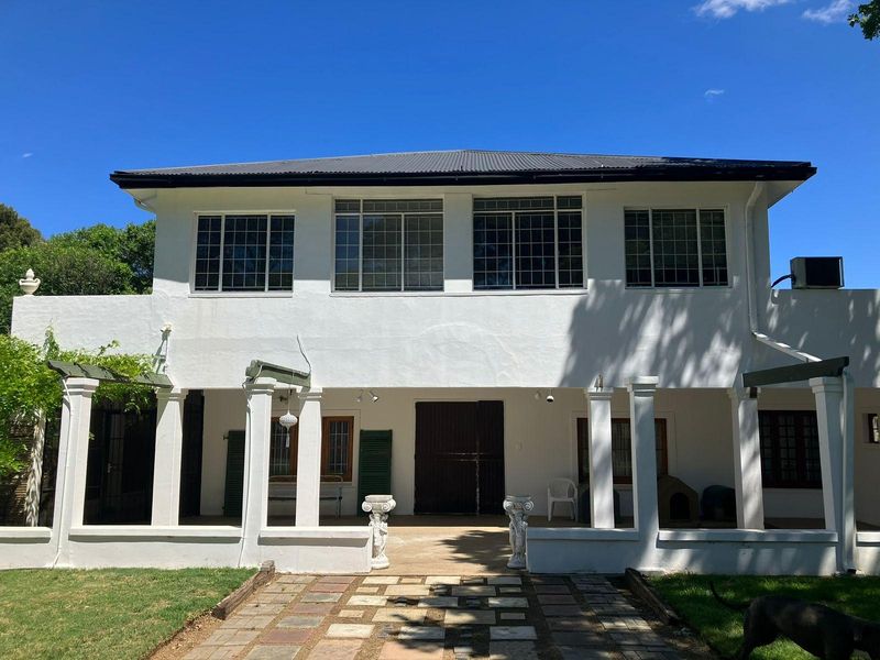 Rear elevation of a two-story farmhouse featuring a covered patio, grid-pattern windows, and a stone-paved walkway leading to the entrance.