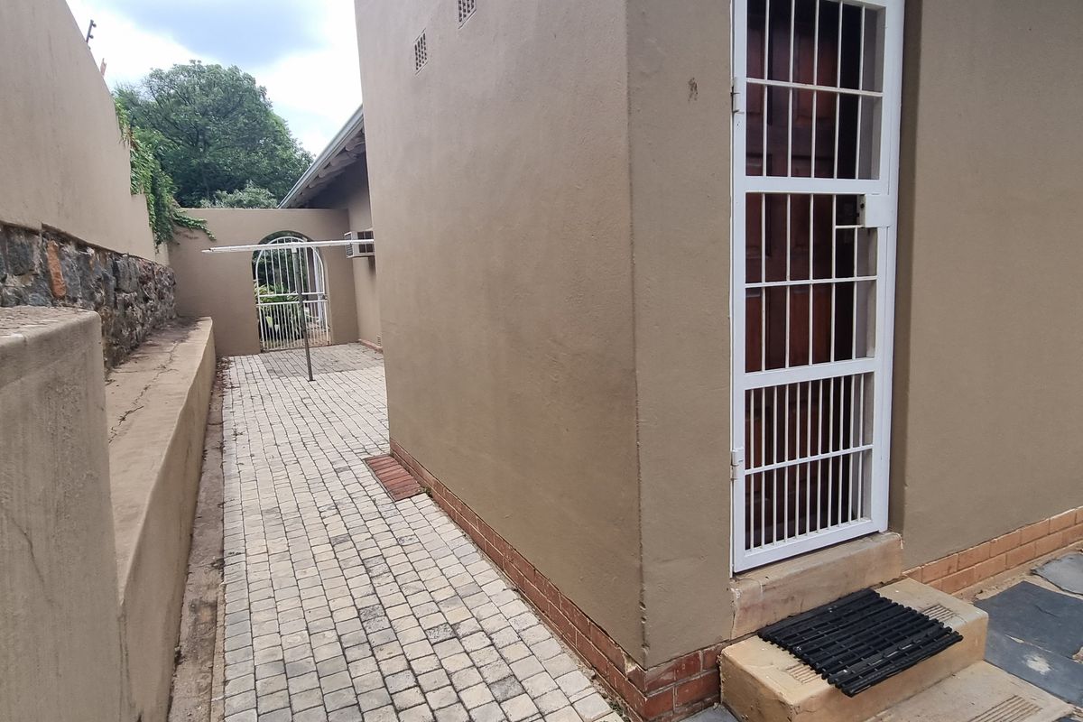 Rear exterior view showing a paved walkway, security gate, and stone retaining wall along the side of the house.